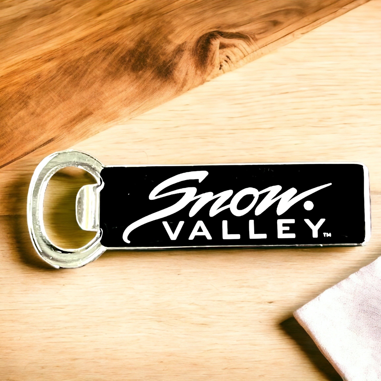 Snow Valley metal bottle opener magnet with black background and white Snow Valley logo design