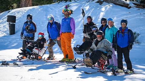 A group of USARC guides in blue jackets and adapative skiers at the top of a Bear Mountain chairlift posing for the camera.