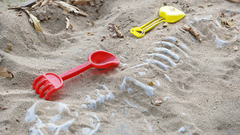 Yellow and red shovel on top of sand, with a bone fossil being uncovered