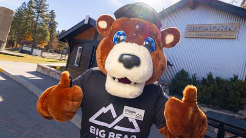 Biggie the Bear mascot in front of Bighorn Smokehouse on a sunny day.