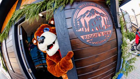 Biggie the Bear mascot peeking out the door of Biggie's Den in the Snow Summit base area.