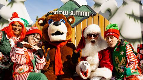 Big Bear Mountain Resort mascot, Biggie, sitting on a large Snow Summit chair with Santa and his little helpers during a sunny winter day.