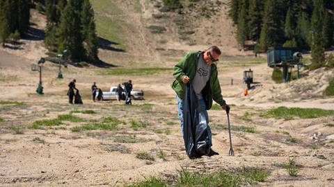 Adult holding a trash bag and trash claw device picking up trash on the summer trails at Snow Valley.