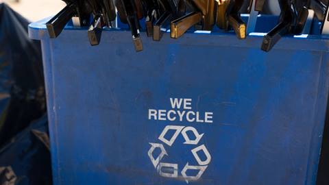 Blue trash bin with the words "We Recycle" and a recycle logo in white on the front and black trash pick up devices placed inside the bin.