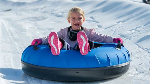 A smiling child in a tube flying down a tube lane at Coyote Creek Tube Park at Snow Valley