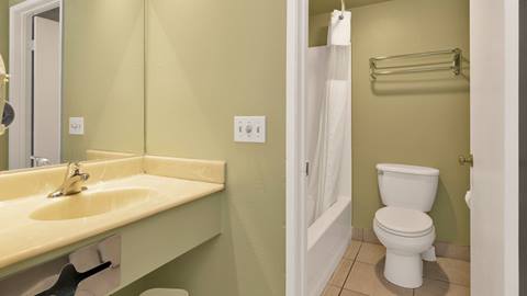 A wash room with sink and bathtub shower combo that has a toilet next to it.
