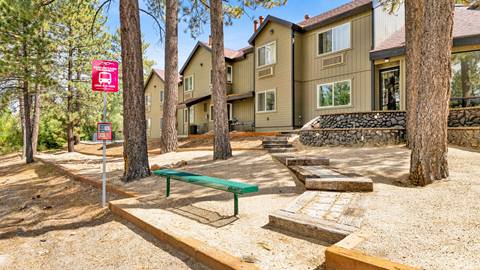 A front view of the employee housing building with a red bus stop, green bench, and pine trees.