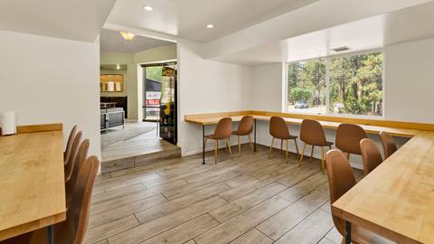 Inside an employee housing common area with tables and chairs for eating and hanging out with window views to the forest.