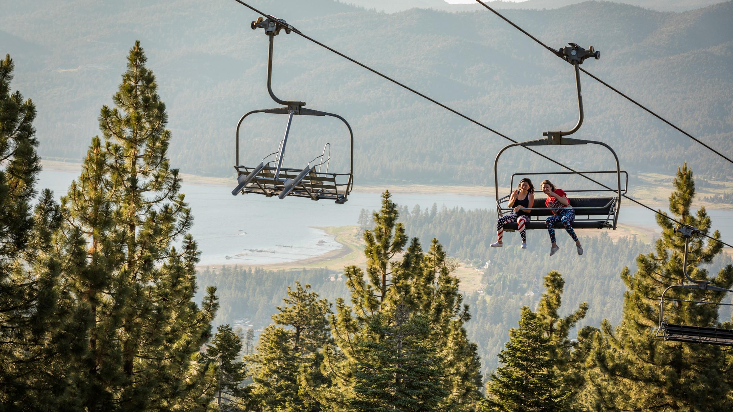 Two people riding the scenic sky chair with big bear lake in the background