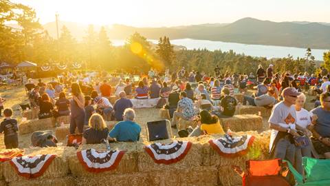A large group of crowd goers sitting in foldable chairs and haybales enjoying sunset at the top of Snow Summit for the annual Above the Boom firework event. 