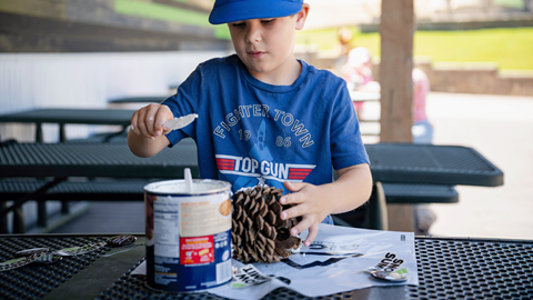 Young kid wearing a blue shirt making a pinecone bird feeder