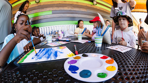 Children painting with colorful watercolors and paint palettes during a summer arts and crafts event at Biggie's Adventure Outpost in Big Bear Mountain Resort.