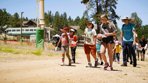 A group of children and camp counselors walking together along an outdoor trail during a summer camp event at Biggie's Adventure Outpost in Big Bear Mountain Resort.