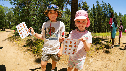 Three smiling children standing outside on a sunny day during a summer youth activity at Biggie's Adventure Outpost at Big Bear Mountain Resort.