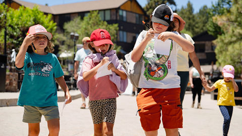 A group of children and camp staff smiling together outdoors while showing off custom white t-shirts at Biggie's Adventure Outpost at Big Bear Mountain Resort.