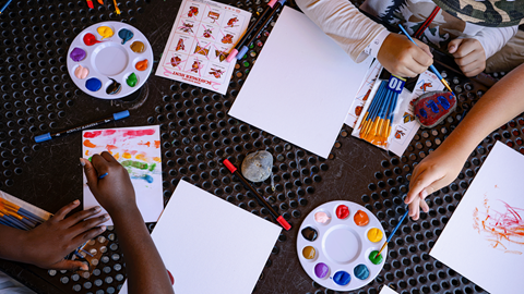 Children painting small wooden birdhouses with colorful paints at picnic tables during an outdoor summer youth camp activity at Biggie's Adventure Outpost at Big Bear Mountain Resort.