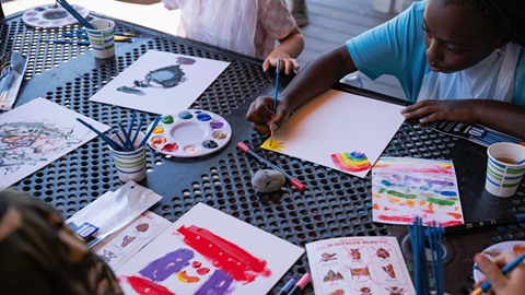 A close-up of a child painting with colorful watercolor palettes during an outdoor summer youth activity at Biggie's Adventure Outpost at Big Bear Mountain Resort.