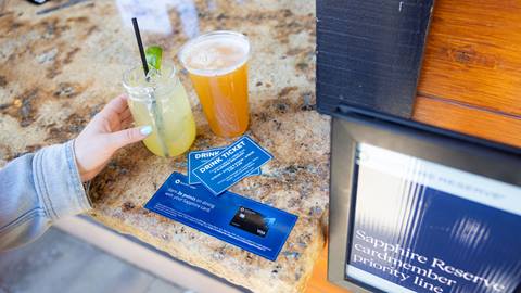 Adult hand grabbing two drinks on bar counter with drink vouchers on display.