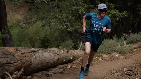 Adult in blue shirt running on dirt path with trees in background