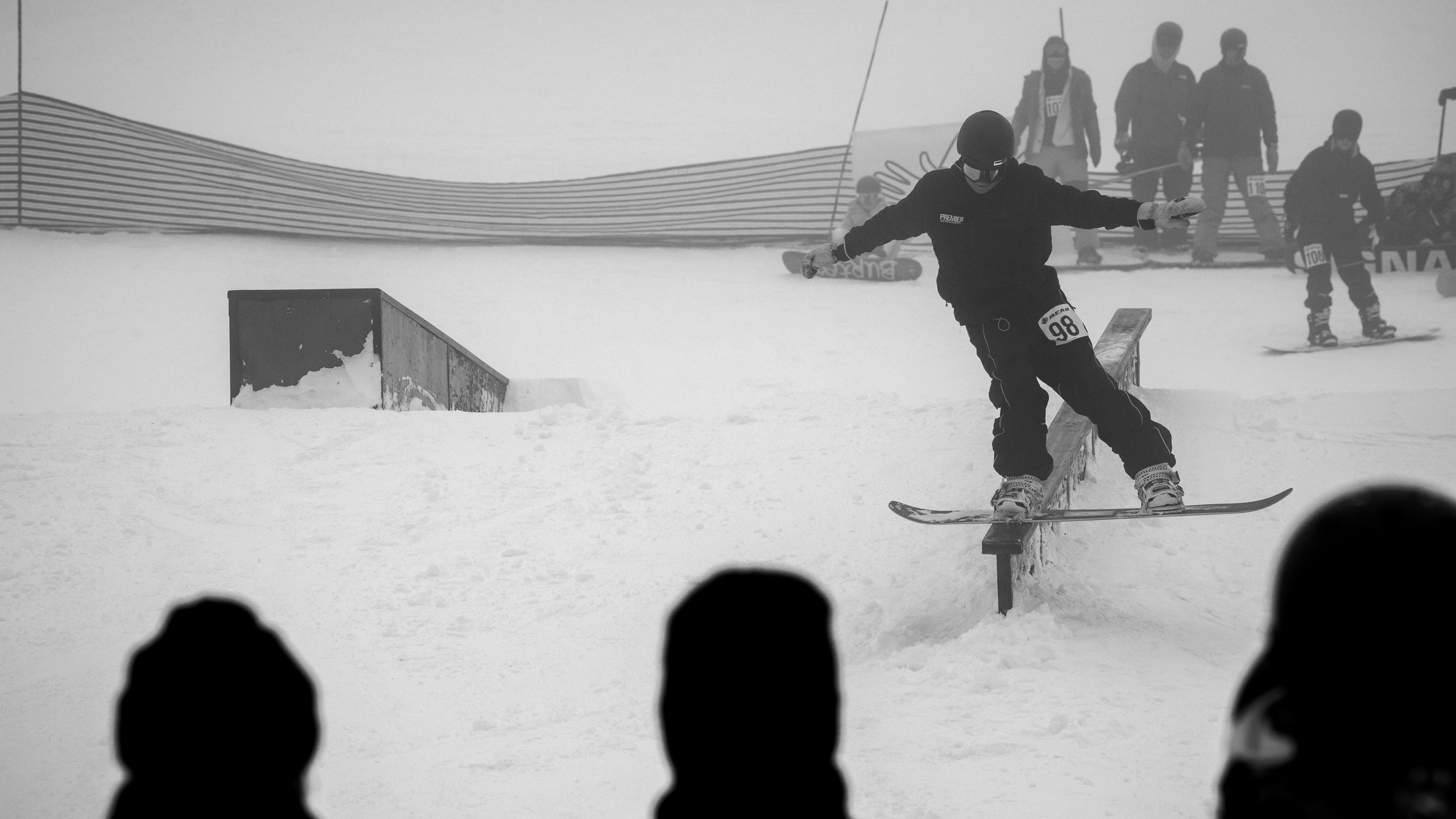 Black and white photo of a snowboarder doing a trick on a snow rail