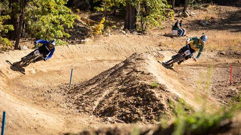 One blue and one yellow cyclist side by side racing through dirt biking berm