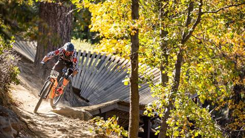 Cyclist with orange bike coming out of a wooden berm riding on dirt path