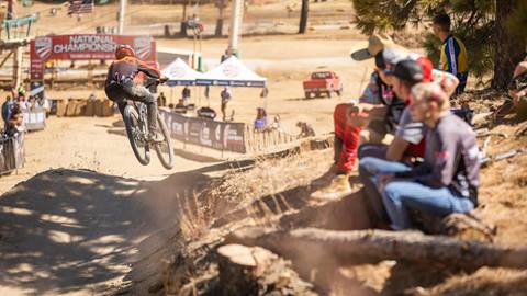 Crowd watching cyclist mid-air fly down dirt jump