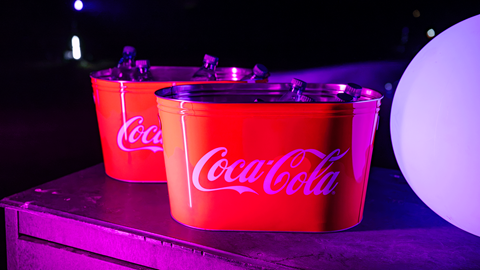 Branded Coca-Cola buckets illuminated by vibrant purple neon lighting on the grass during the Driving Range After Dark event at Big Bear Mountain Resort.