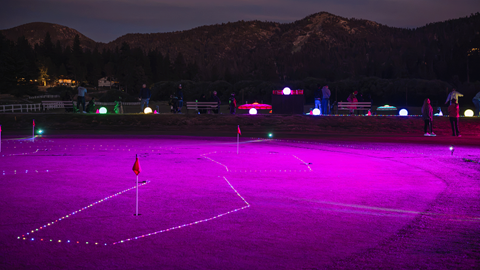 Wide evening view of the driving range outfield brightly illuminated with vibrant purple and pink neon lights during the Driving Range After Dark event at Big Bear Mountain Resort.