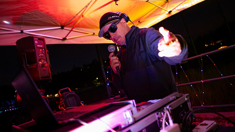 A DJ performing on a stage with neon pink and purple lighting at Big Bear Mountain Resort's Driving Range After Dark evening event.