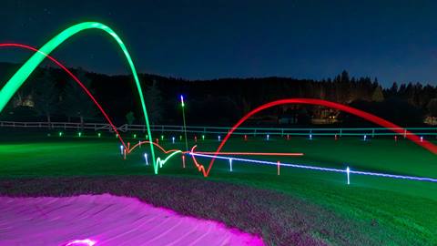 Red, green, and blue glow golf balls bouncing along a putting green with a lit up purple sand bunker in the bottom left corner