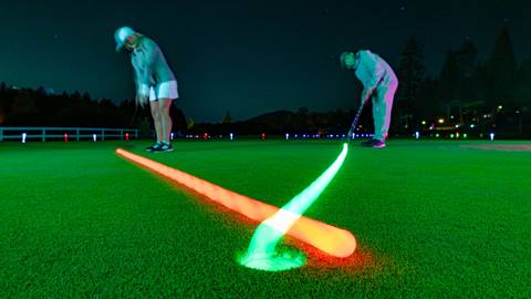 Two adult golfers at night putting glow in the dark colorful balls into the hole at Bear Mountain Golf Course