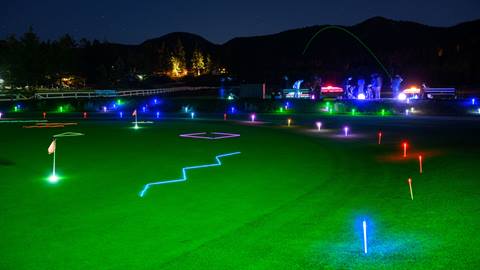 Bear Mountain Golf Course's driving range and putting area illuminated at night with different colored lit up lights to enhance a glow range experience.