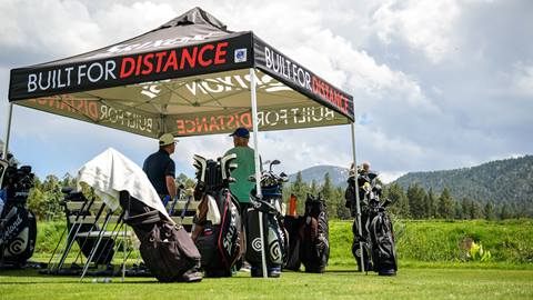 two guys talking to each other under a black tent on the grass with a table and golf clubs during the Bear Mountain club demo event in the summer