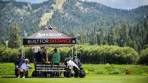few males under a black tent on the grass with a table and golf clubs during the Bear Mountain club demo event in the summer with the ski resort in the background