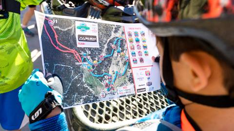 A kiddo with a helmet and bike gloves, holding a Kids Adventure Games map that shows the layout of the Bear Mountain course.