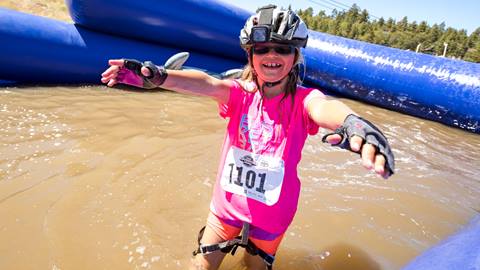 A kiddo in a helmet, black sunglasses, and a pink shirt, standing in a pool of water during the Kids Adventure Games.
