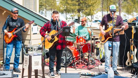 Four musicians, including three guitarists and a drummer, playing live music at Snow Valley on the sun deck