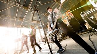 Two guitarists and a bass player in all black clothing on a stage playing live music.