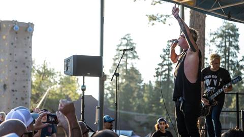 A band playing live music in the base area at Snow Summit, with a rock climbing wall in the background, playing for a crowd during the summer.