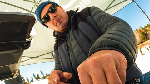 DJ Slipmatt behind his DJ setup, under a Big Bear Mountain Resort black eazeup tent, performing at a ski resort in the base area on a sunny winter day.
