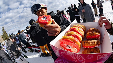 Snowboarder grabbing a red donut out from a box and showing the camera