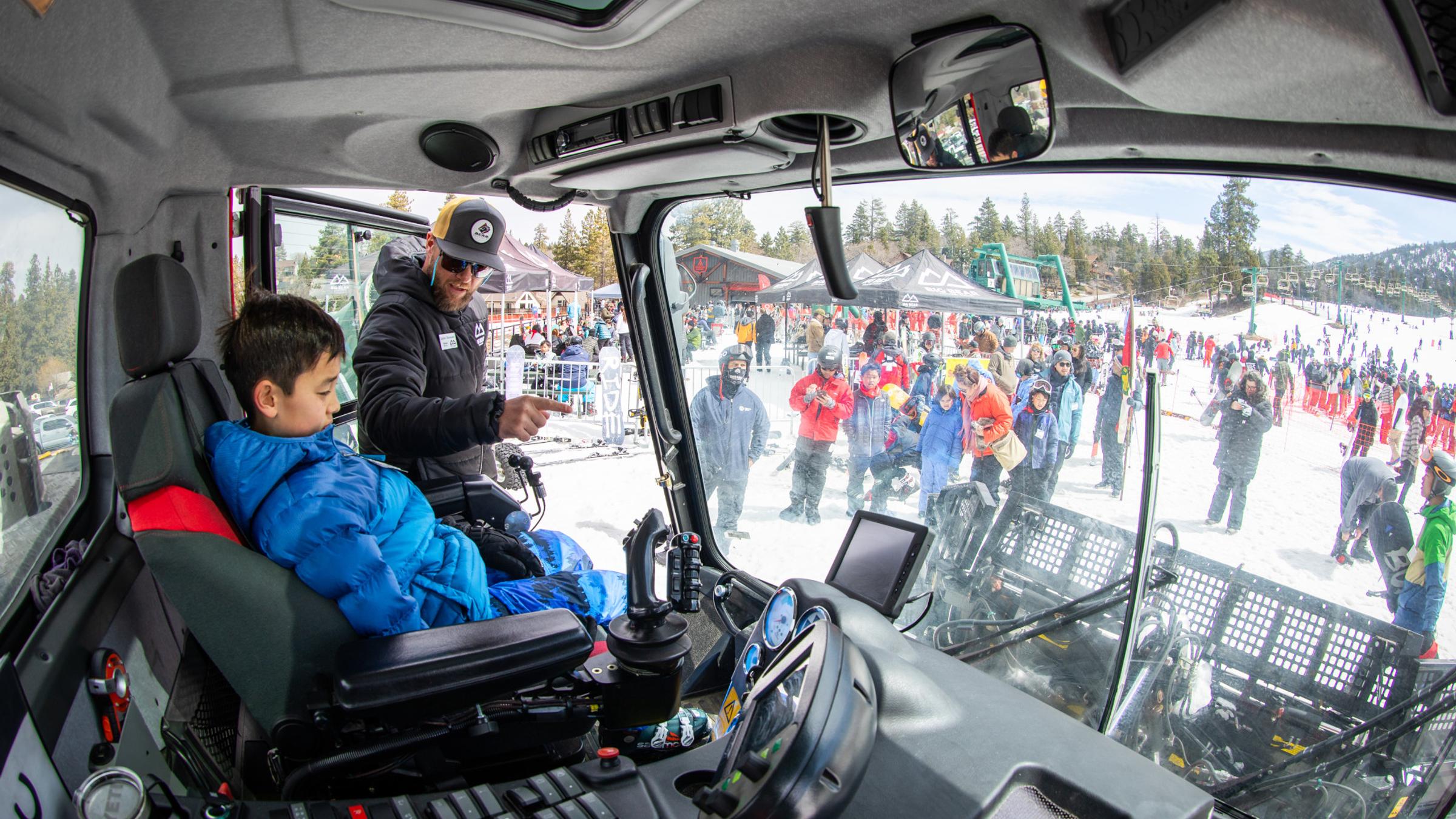 Kid in a machinery truck learning from a snow instructor