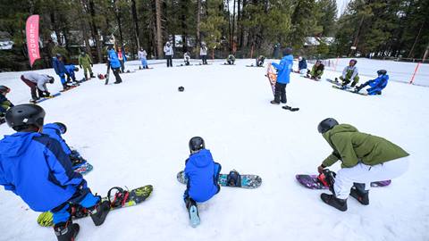 A large group of snowboarders and Big Bear Mountain Resort snowboard instructors in a circle getting ready for their lessons