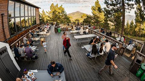 Guests on the deck of Skyline Taphouse at Snow Summit during an evening summer event with food and beverage.
