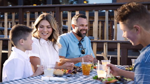 Mom, dad, and two sons talking to each other at a dinner table during Skyline at Sundown at Snow Summit in the summer