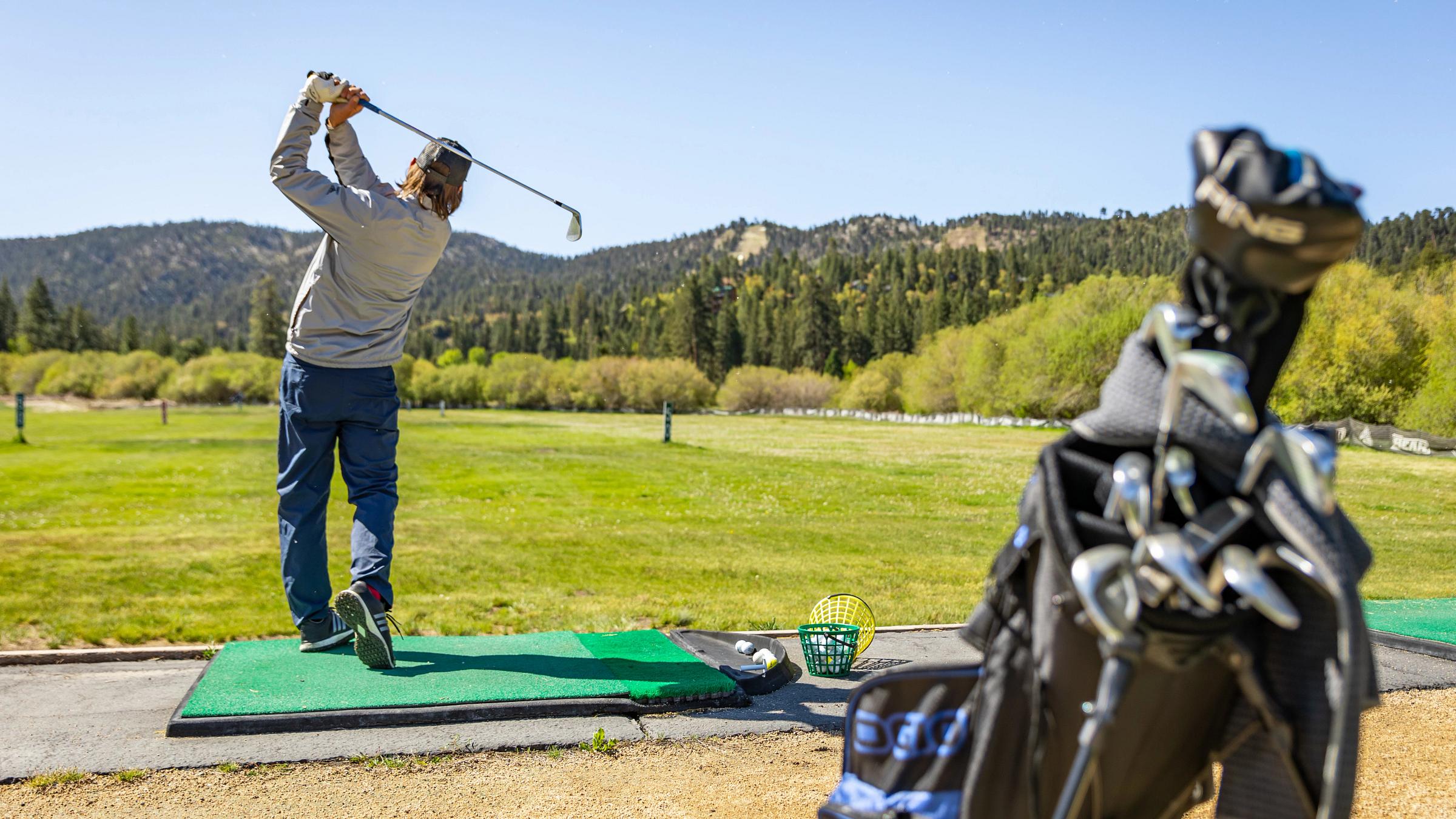 Guy in grey shirt hitting a golf ball at the Bear Mountain Golf Course Driving Range