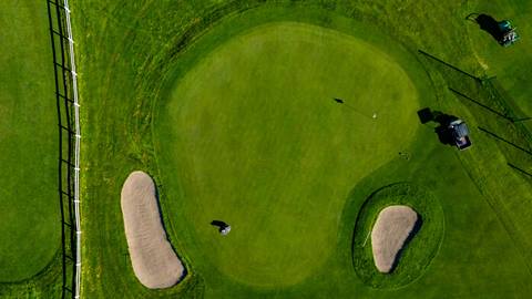 Drone view of a putting green with two sand bunkers and two lawn mowers, at Bear Mountain Golf Course during the summer season.