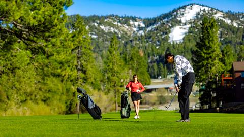Two golfers at Bear Mountain Golf Course playing a round on the lush green course, with a melting ski trail on Bear Mountain in the distance.a