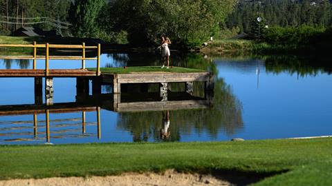 Adult golfer in a white golf dress at Bear Mountain Golf Course on the tee box for Hole 8, which is surrounded by a water hazard.